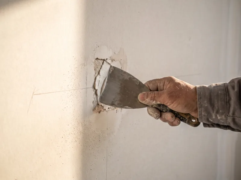 A hand pressing filler into a small wall repair with a broad taping knife